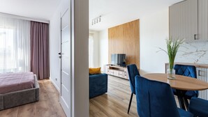 Une chambre d’hôtel moderne équipée d’un lit, d’une télévision, d’un coin repas avec des chaises et d’un plancher en bois.