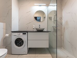 Un bany modern amb rentadora, un lavabo amb mànega, un mirall i dutxa amb envàs de vidre.