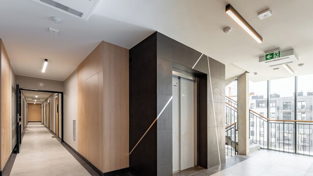 Un couloir moderne avec un mur en bois, un mur d’accent noir et un ascenseur en verre.