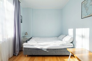 Ein Schlafzimmer mit Bett, Nachttisch, Lampe, einer Karte an der Wand und einem Fenster mit Vorhängen.