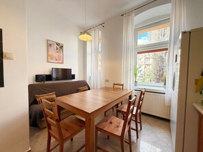 Un comedor con una mesa y sillas de madera, un televisor en la pared, un sofá y una ventana con cortinas.