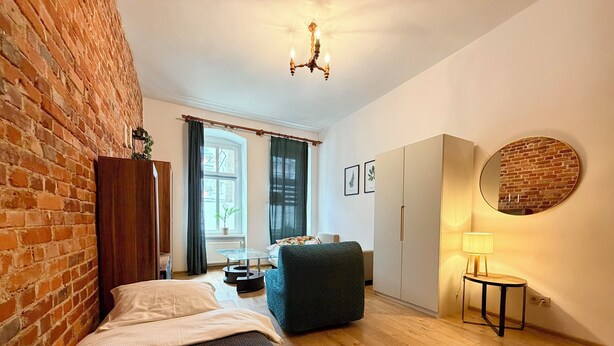A bedroom with a brick wall, a bed, a wardrobe, a mirror, and a small table with a lamp. - Daszyńskiego Spacious Apartment (Wrocław)