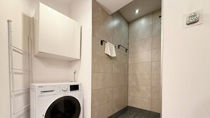 A laundry area with a washing machine, a towel rack, and a shower stall with tiled walls. - Chrobrego Modern Style Apartment (Wrocław)