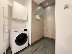 A laundry area with a washing machine, a towel rack, and a shower stall with tiled walls. - Chrobrego Modern Style Apartment (Wrocław)