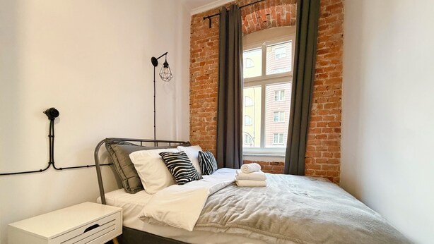 Ein modernes Schlafzimmer mit Backsteinwand, einem Bett mit weißer Bettwäsche, einem Nachttisch und einer Wandlampe.