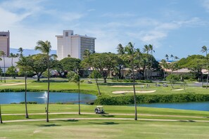 A golf course with a water feature, palm trees, and buildings in the background. - Spacious 2BR Condo w Lanai Near Beach & Dining - Kaanapali Royal E101 (Lahaina)