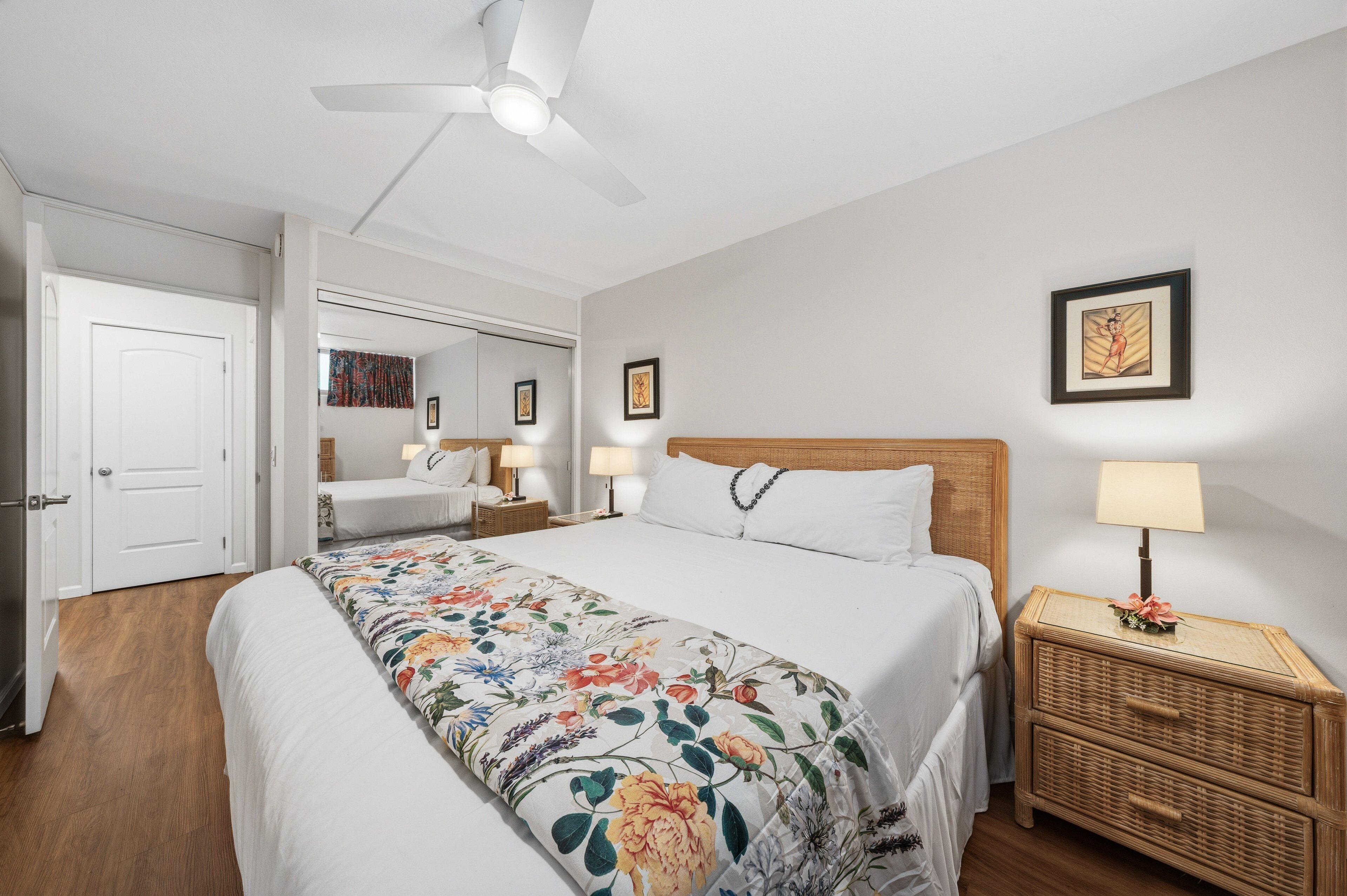 Une chambre à coucher comprenant un lit, des tables de chevet, un ventilateur de plafond et une porte donnant sur une autre pièce.