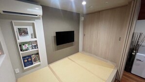 Una habitación con suelo de esteras de tatami, televisor montado, estante con objetos y armario.