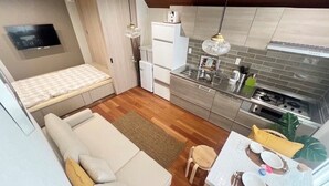 Un espacio habitable compacto con kitchenette, un sofá, una mesa de comedor y un televisor montado en la pared.