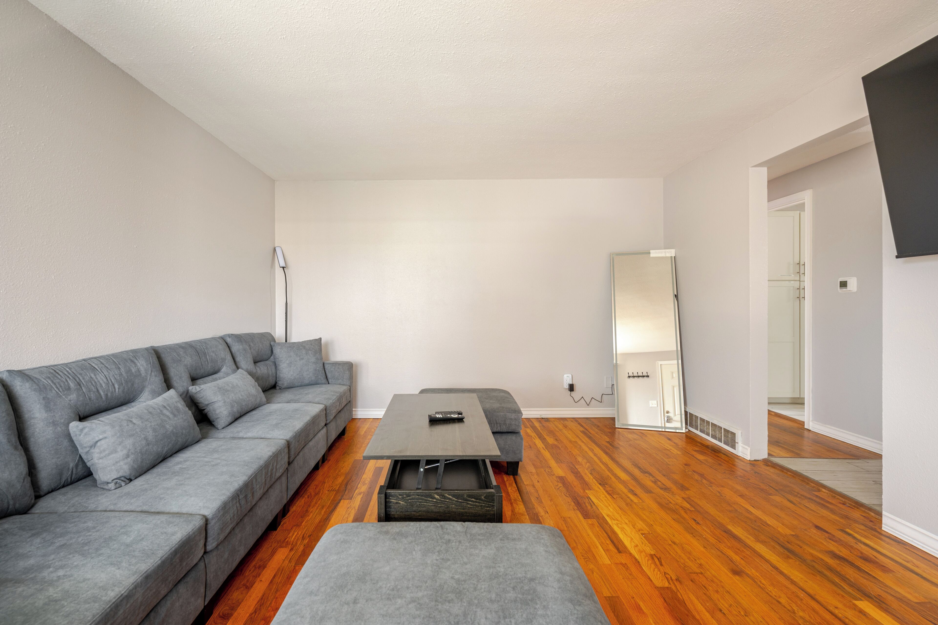 Una sala de estar moderna con un sofá gris, una mesita y piso de madera.