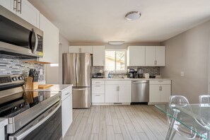 Una cocina moderna con electrodomésticos de acero inoxidable, armarios blancos y una mesa de comedor de vidrio.