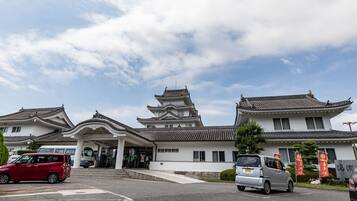 A traditional Japanese building with multiple tiers and a white facade, located at a street intersection with cars parked in front.