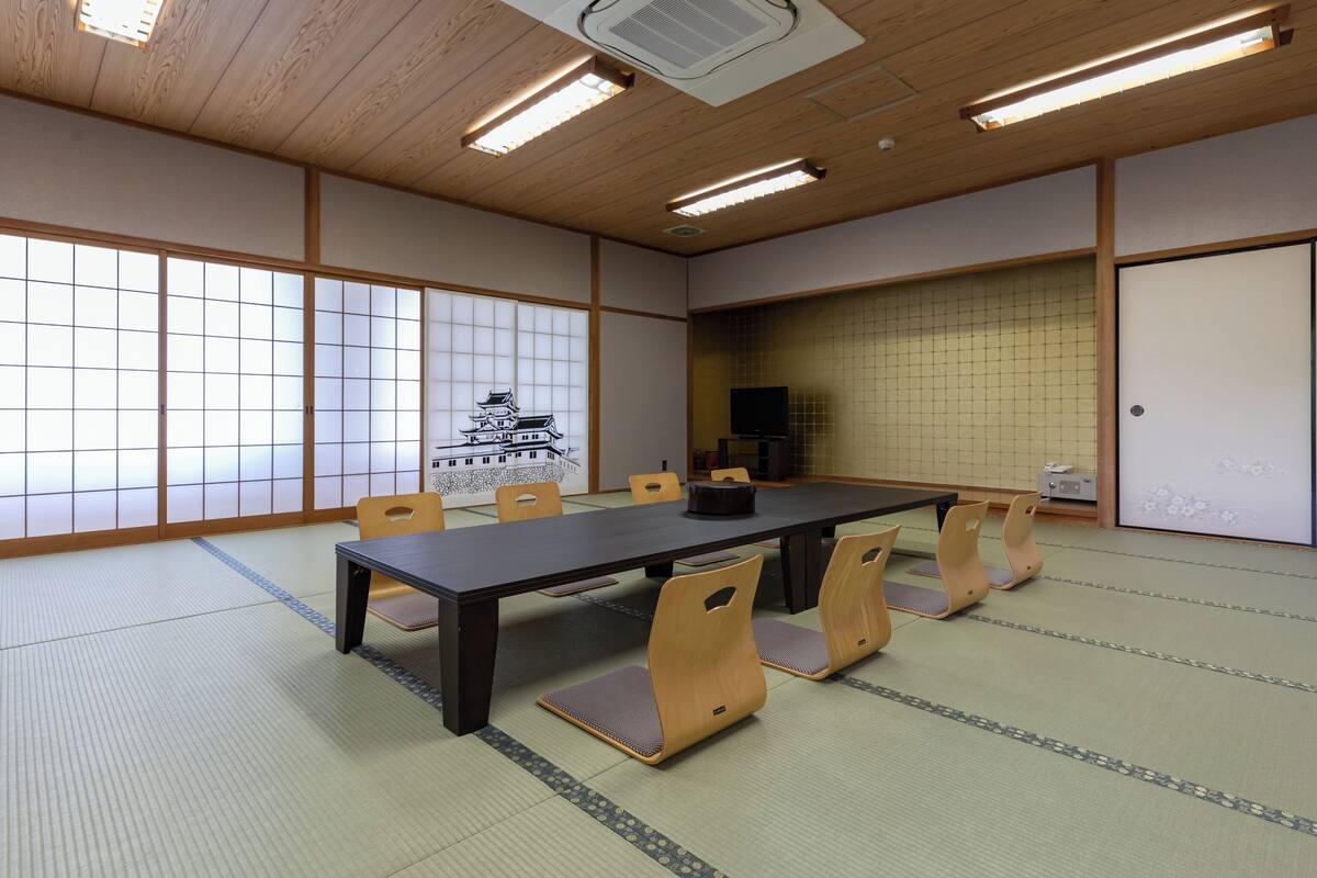 A traditional Japanese-style room with tatami flooring, a low table with chairs, a television, and a sliding door.