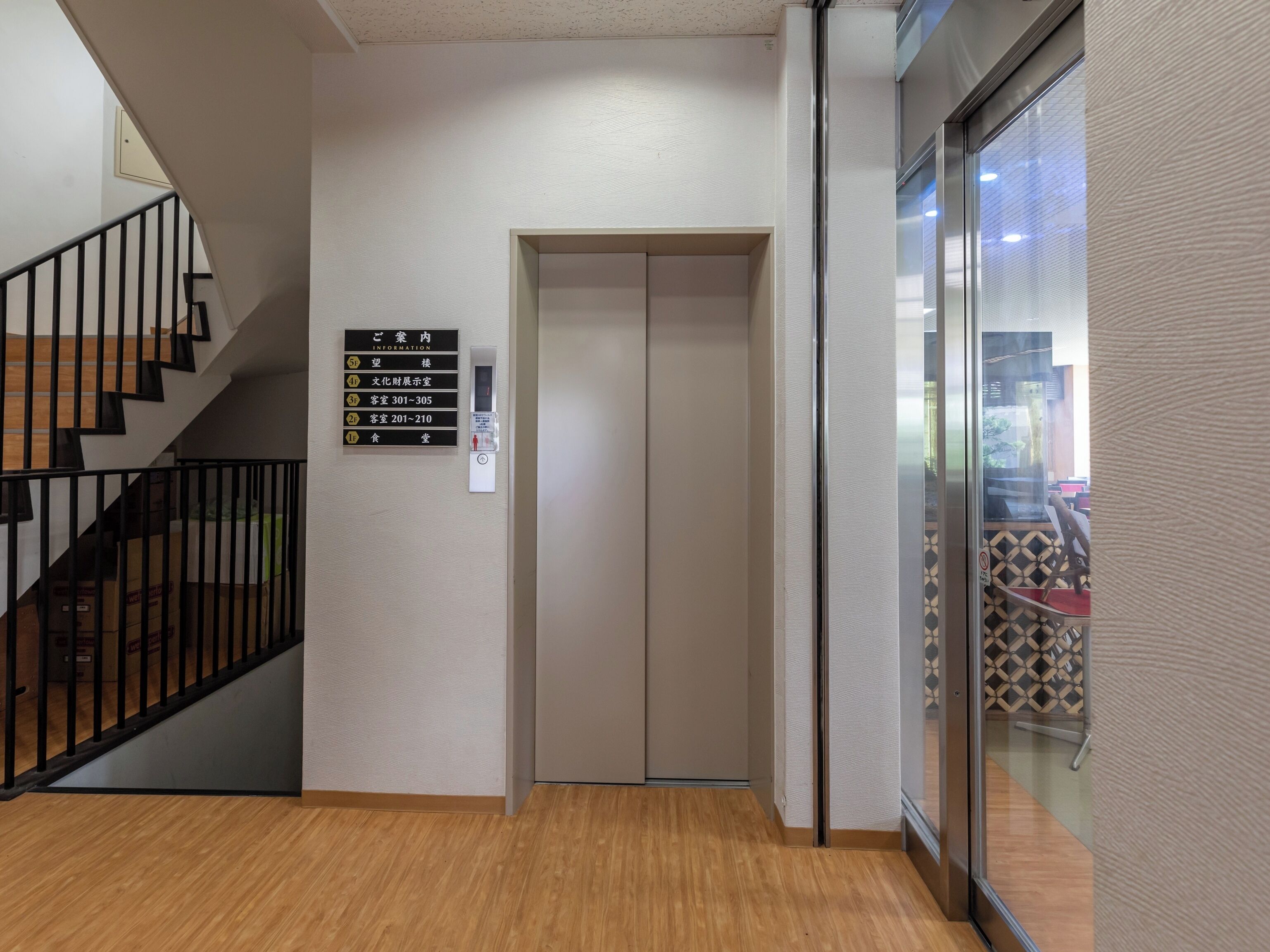Un ascenseur avec une signalétique indiquant les numéros des chambres et un escalier muni d’une rampe.