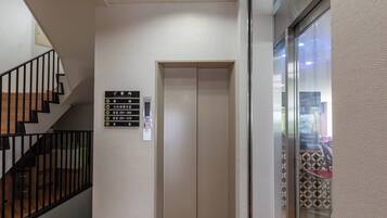 Un ascenseur avec une signalétique indiquant les numéros des chambres et un escalier muni d’une rampe.