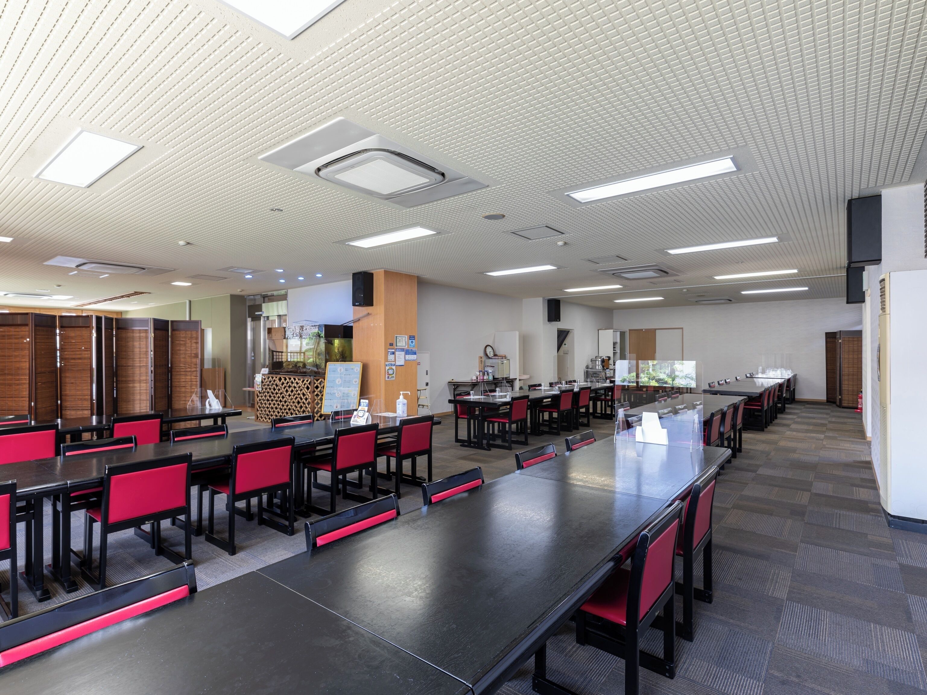A conference room with multiple tables and chairs, a wooden partition, and a white ceiling with recessed lighting.