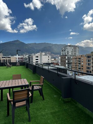 Eine Dachterrasse mit Kunstgrasanlage, Sitzmöbeln und Blick auf die Stadt.