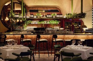 Una zona de bar con encimera de mármol, botellas de vino, copas y plantas en macetas.