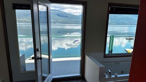 Ein Badezimmer mit großem Fenster mit Blick auf einen See und Berge, einer Badewanne und einem Hund im Vordergrund.
