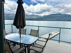 A table and chairs on a balcony with a view of a lake and mountains.