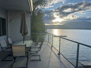 A balcony with a table and chairs, overlooking a body of water with mountains in the distance.
