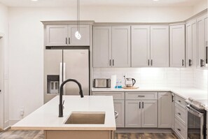 A modern kitchen with grey cabinets, a stainless steel refrigerator, a built-in microwave, and a sink with a black faucet. - Luxurious New Construction 4-bedroom house in charming Decatur (Decatur)