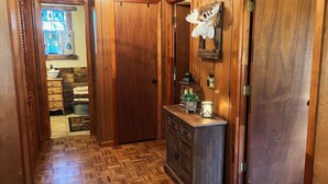 A wooden hallway with a herringbone floor, a wooden door, and a small console table with a lantern and a plant.