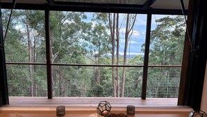 Ein Esstisch mit Tellern, einem Schneidebrett und Kerzen, vor einem großen Fenster mit Blick auf einen Wald.