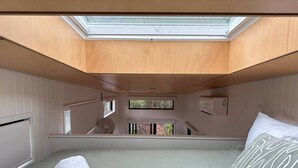 Ein gemütliches Schlafzimmer mit Dachfenster, einem Bett mit gemustertem Kissen und Blick auf eine grüne Umgebung.