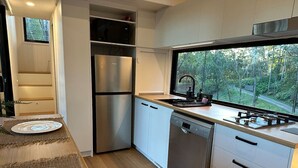 Eine moderne Küche mit eingebautem Geschirrspüler, Edelstahlgeräten und einem Fenster mit Blick auf einen Wald.