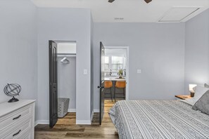 Ein Schlafzimmer mit Bett, Schminktisch, Schreibtisch und Stuhl. Eine Tür führt zu einem Badezimmer und einer Küche.