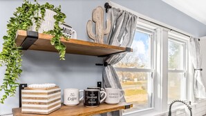 Een keuken met een houten plank, een cactusdecoratie, een raam met gordijnen en een koffiemok met tekst.