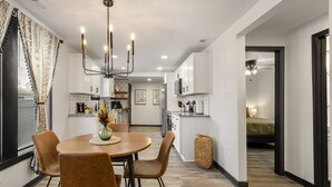 Une cuisine moderne avec des meubles blancs, un coin repas avec une table ronde et des chaises, et un lit visible dans la pièce adjacente.