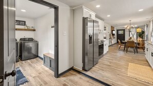 Une cuisine moderne équipée d’appareils électroménagers en acier inoxydable, un coin repas avec une table et des chaises en bois, et une buanderie avec un lave-linge et un sèche-linge.