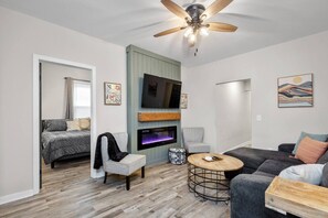Una sala de estar moderna con televisor de pantalla plana, ventilador de techo, chimenea y un rincón de descanso acogedor.