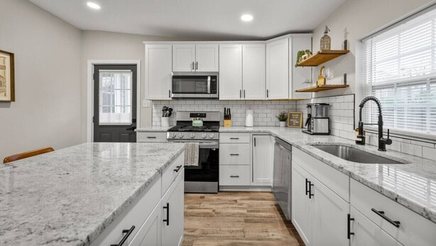 A kitchen with white cabinets, a microwave, a stove, a sink, and a wooden floor. - Church Hill Hideaway #1 | 3 BR Backyard Oasis (Richmond)
