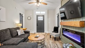 A living room with a sofa, coffee table, TV, fireplace, and ceiling fan. - Church Hill Hideaway #1 | 3 BR Backyard Oasis (Richmond)