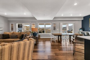 Un vaste espace de vie comprenant un canapé, une table à manger et des chaises, un coin cuisine et de grandes fenêtres offrant une vue dégagée.