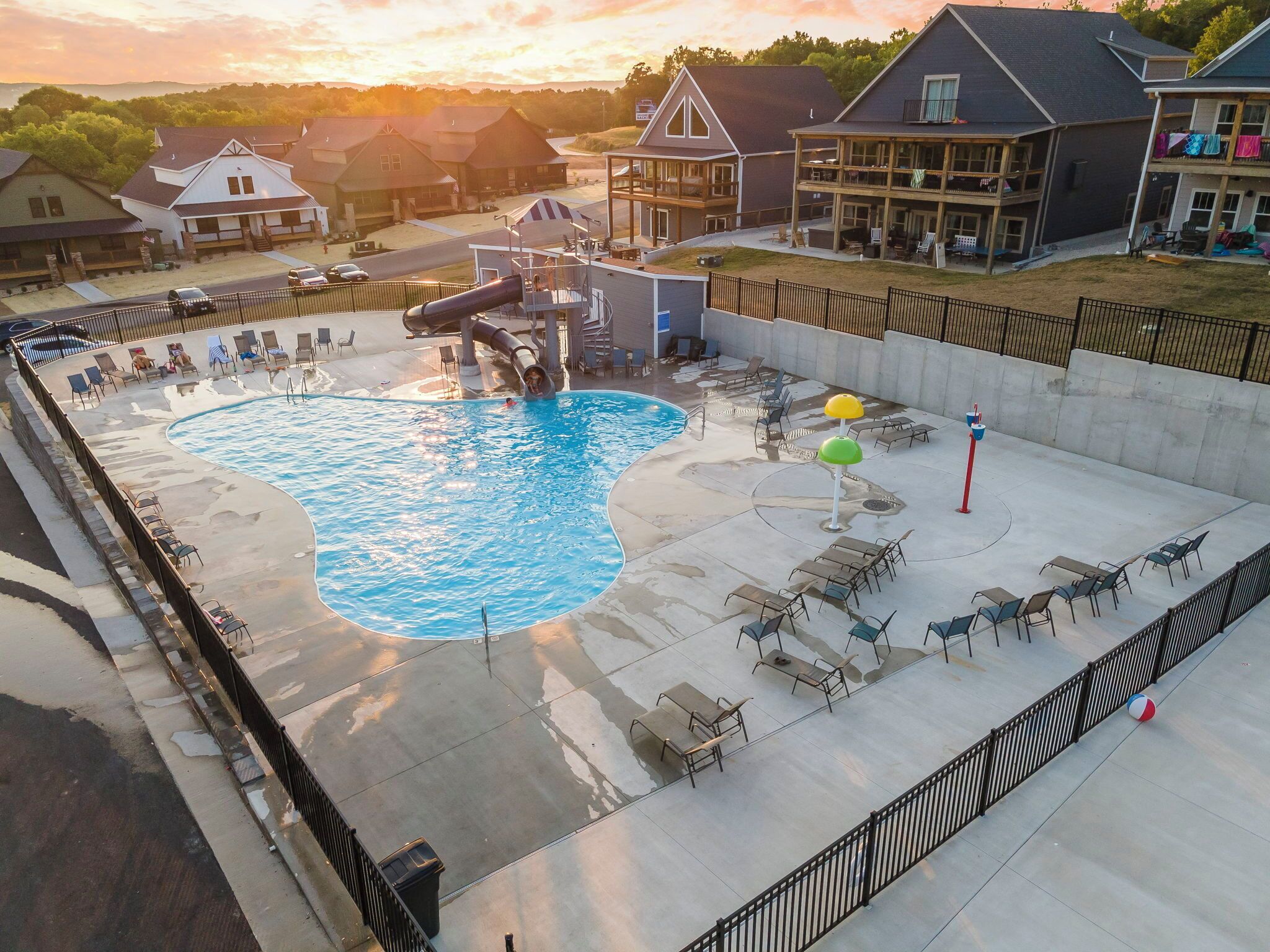 A swimming pool with a water slide, lounge chairs, and umbrellas.