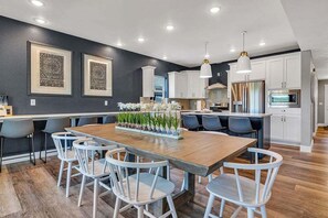 Une cuisine moderne avec des meubles blancs, des appareils en acier inoxydable et une table à manger en bois, assortie de chaises blanches.