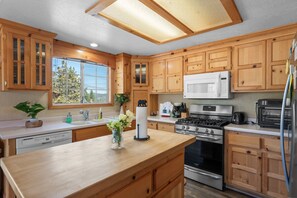 A kitchen with wooden cabinets, a stove, microwave, and a refrigerator. - The Lazy JT Ranch - Slope views, fenced yard, deck, bbq (Big Bear City)