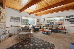 A cozy living room with a stone fireplace, two sofas, a coffee table, and a view of a lake through large windows. - The Lazy JT Ranch - Slope views, fenced yard, deck, bbq (Big Bear City)