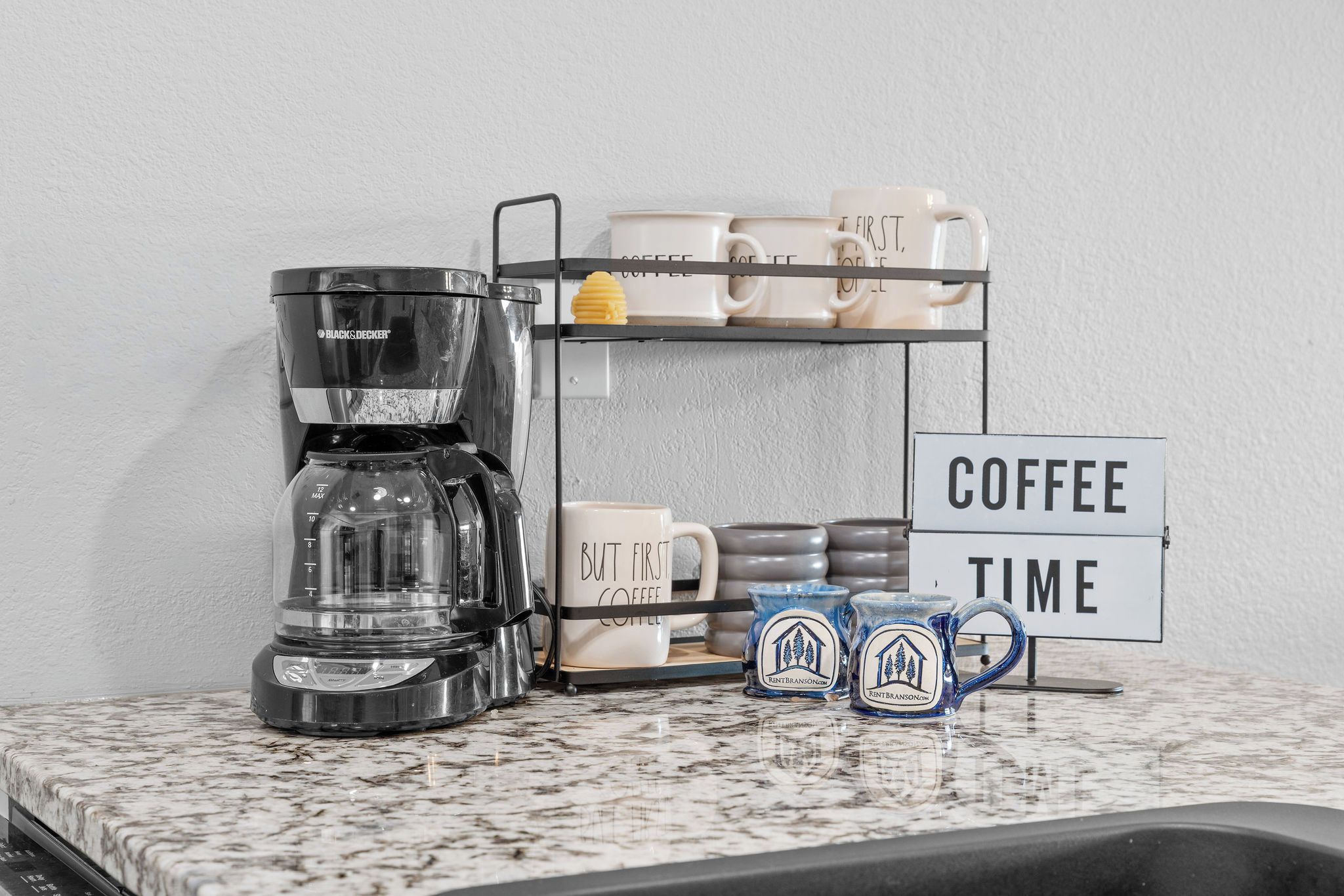 Eine Kaffeemaschine, ein Becherhalter und ein Schild mit der Aufschrift Kaffee auf einer Küchenarbeitsplatte.