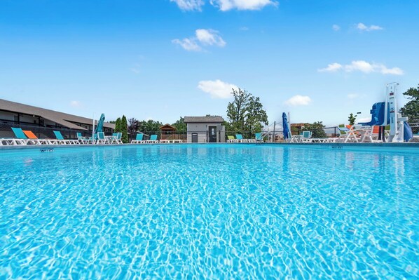 A swimming pool with lounge chairs and umbrellas, a small building, and trees in the background. - Condo in Kimberling City w Lake View_Cmty Pools_Free Attaction Tickets (Kimberling City)