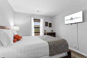 Ein Hotelzimmer mit Bett, Wandfernseher, Vorhängen am Fenster und Blick ins Freie.