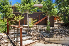 A two-story building with a wooden staircase, a metal gate, and a stone retaining wall. - Honey Bear Cabin - Upper Moonridge | Fireplace + Slope Views (Big Bear Lake)