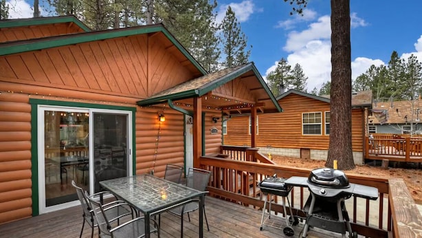 Une cabane en rondins avec une terrasse, une table en verre, des chaises et un barbecue.
