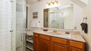Une salle de bain dotée d’une douche à parois de verre, d’un meuble-lavabo double avec des armoires en bois, d’un grand miroir et d’un porte-serviettes mural.