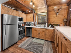 A modern kitchen with stainless steel appliances, wooden cabinets, and a rustic ceiling. - Starlight Lodge - Family-Friendly Gambrel Cabin | 5 Min to Slopes, Lake & Dining (Big Bear City)