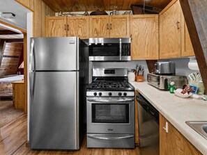 A compact kitchen with a stainless steel refrigerator, a microwave, a stove, and a dishwasher. - Starlight Lodge - Family-Friendly Gambrel Cabin | 5 Min to Slopes, Lake & Dining (Big Bear City)